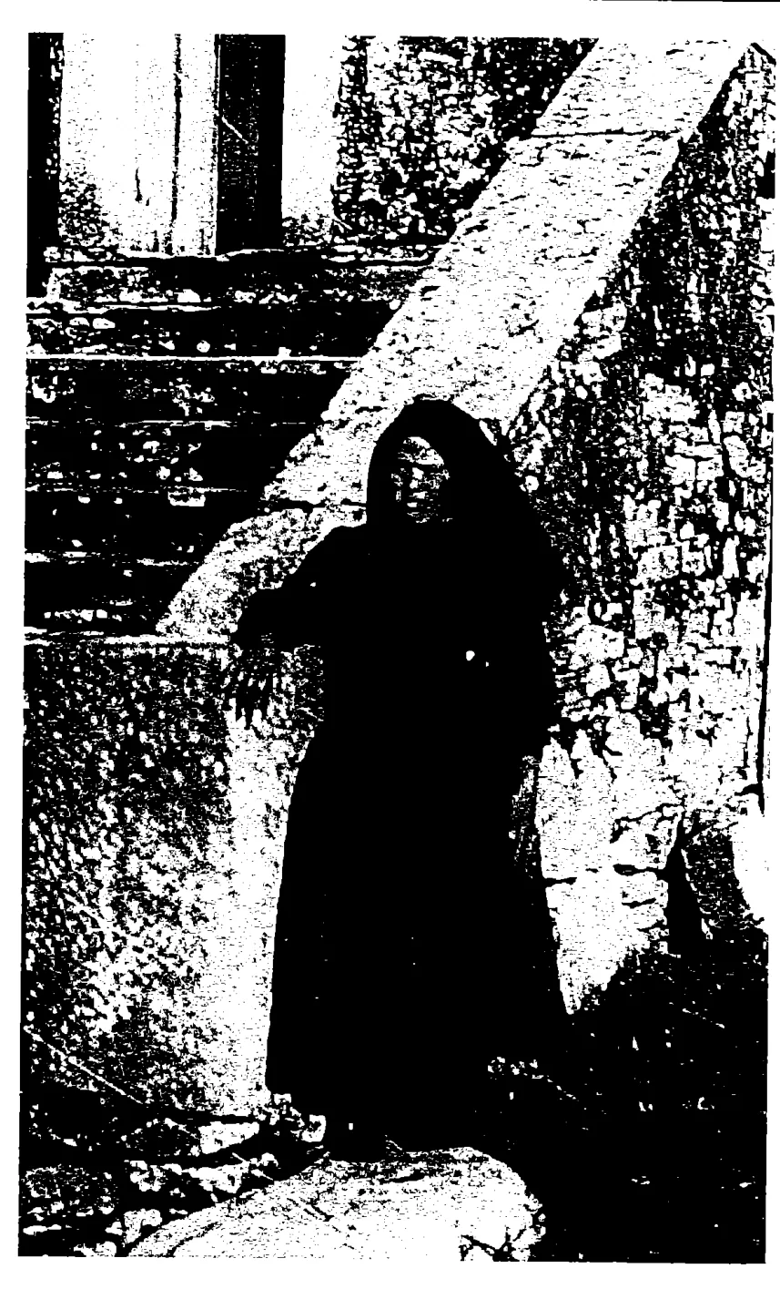 Elderly woman in a black shawl by stone steps: Original scan